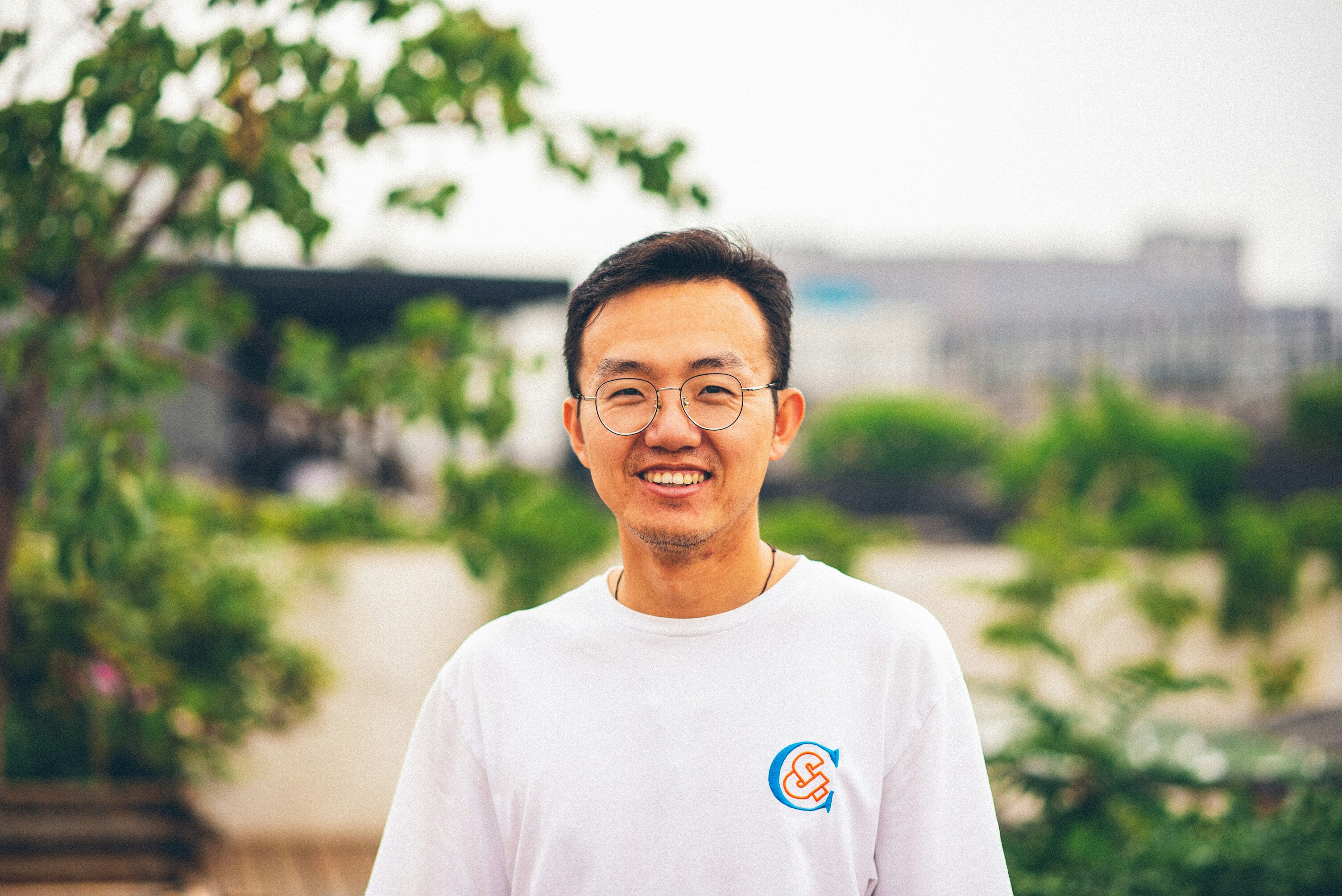 Smiling Asian man in a white T-shirt standing on a green rooftop terrace