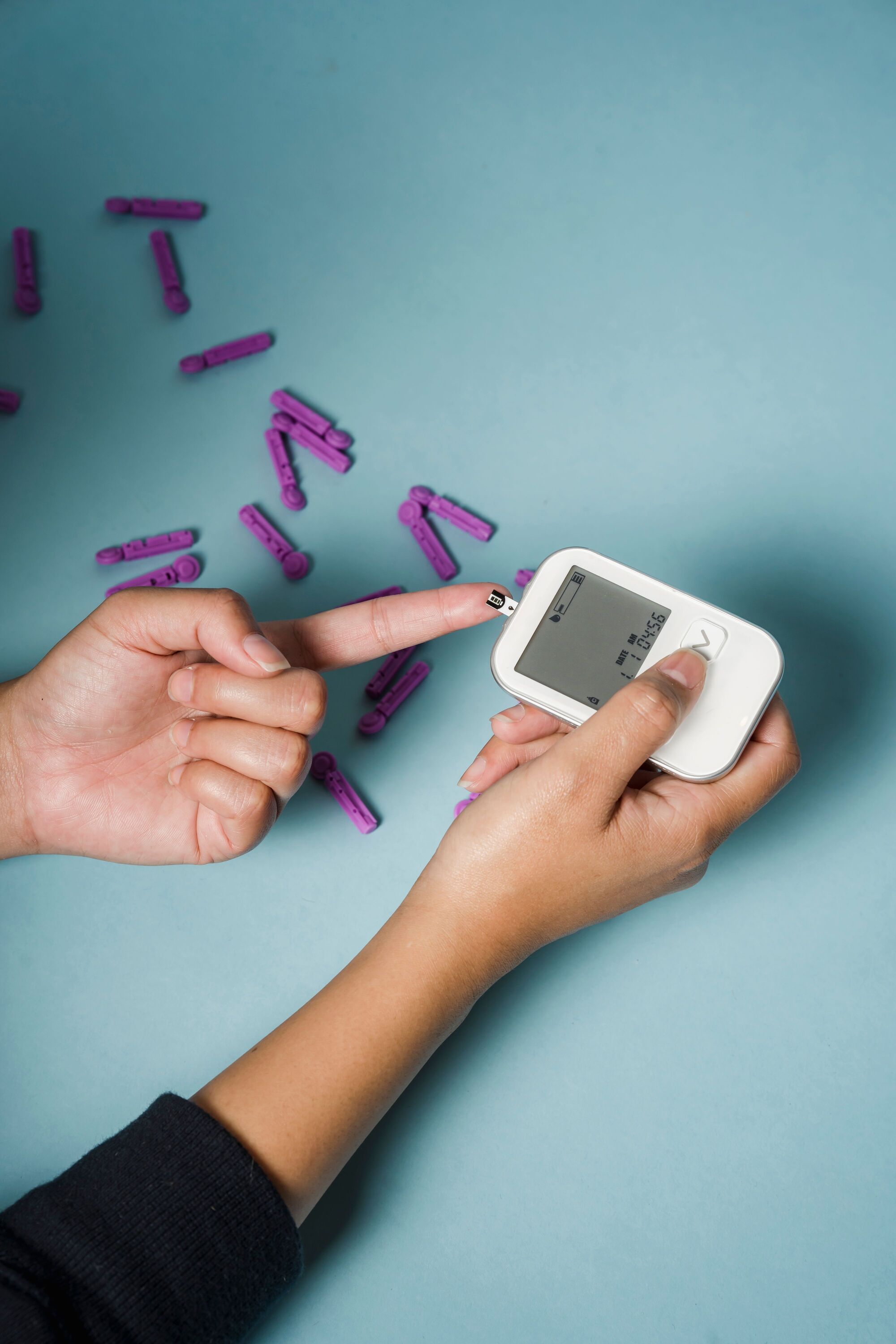 Hands using a glucose meter and a test strip on a blue background